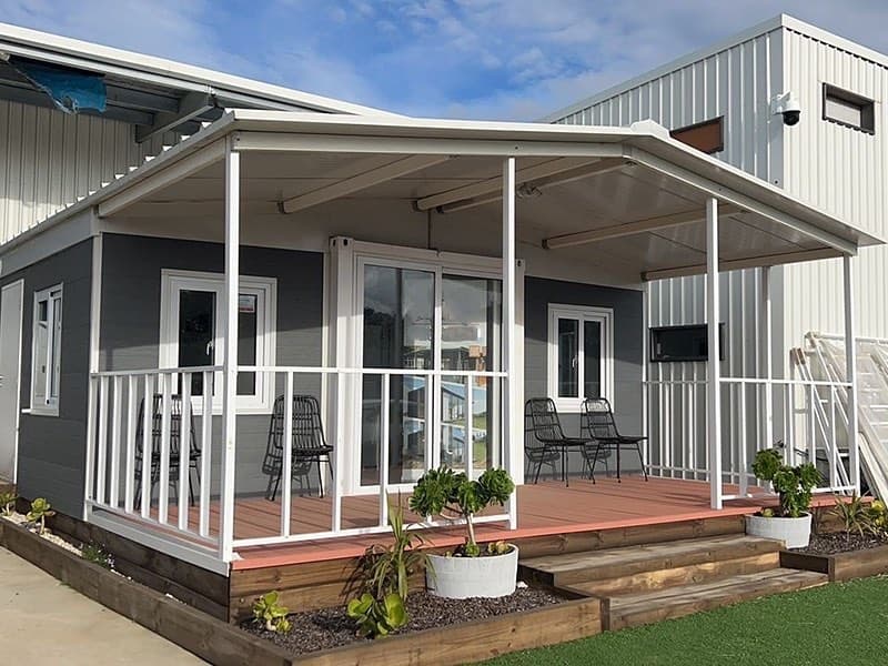 Gray expandable home with a white covered porch and deck.